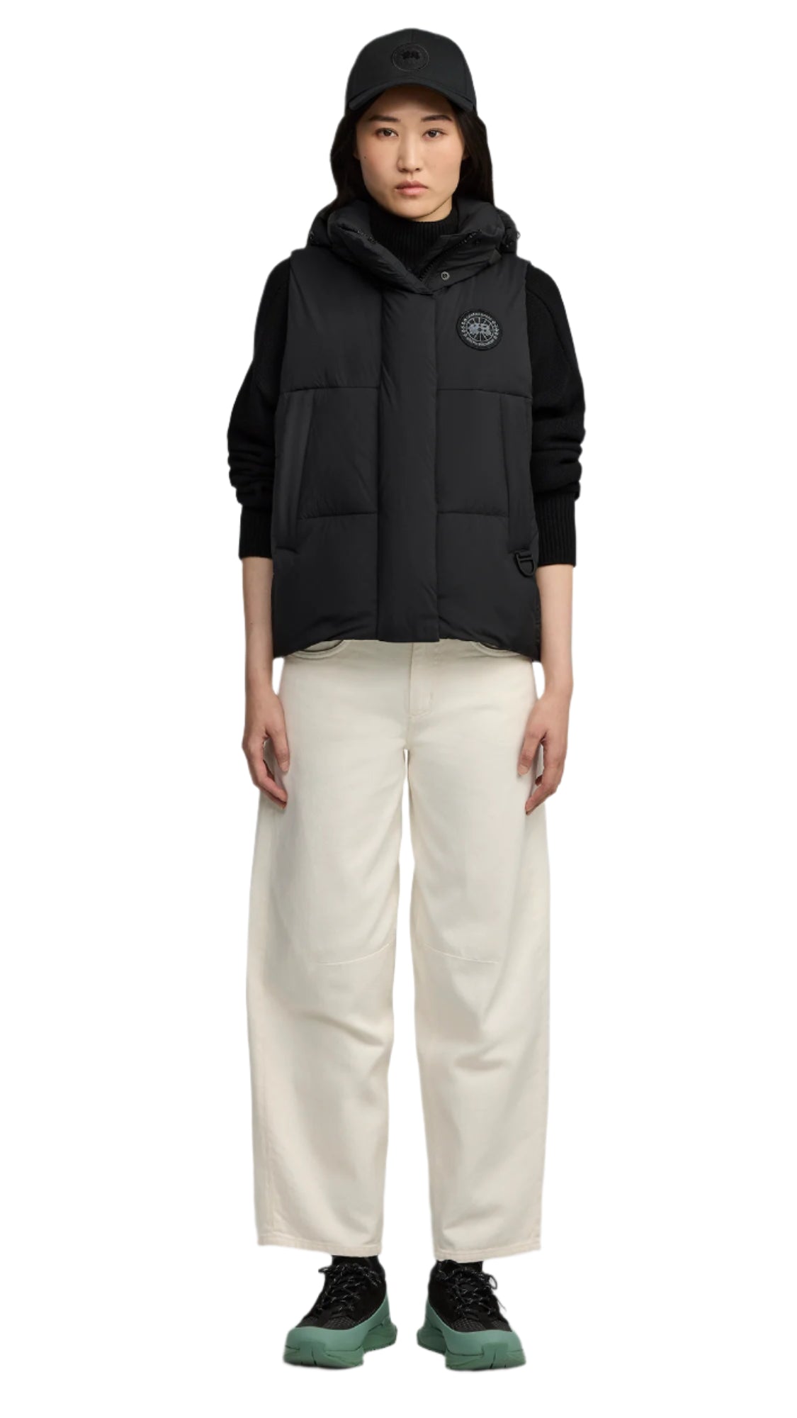 A woman wearing a black vest, black shirt, white pants, black shoes and a black hat.