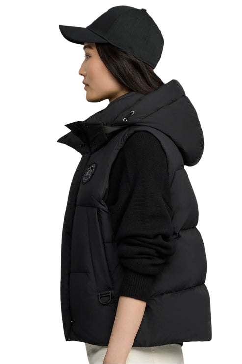 A woman with a baseball cap wearing a black, hooded, puffy vest.