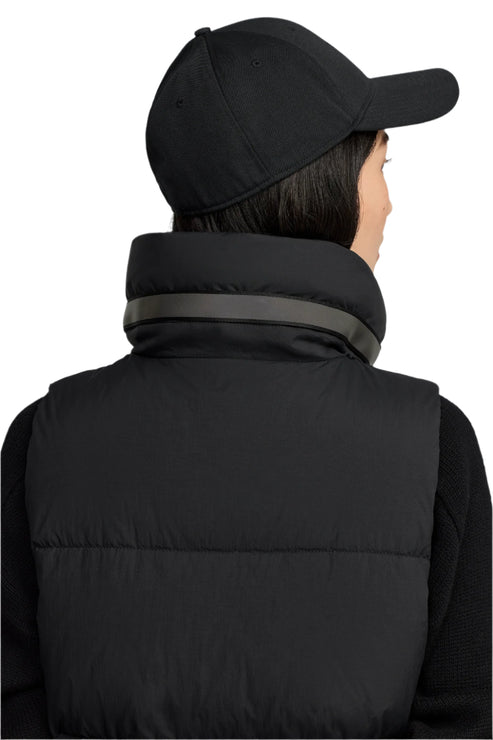 A person wearing a black baseball cap and black puffer vest seen from the back.