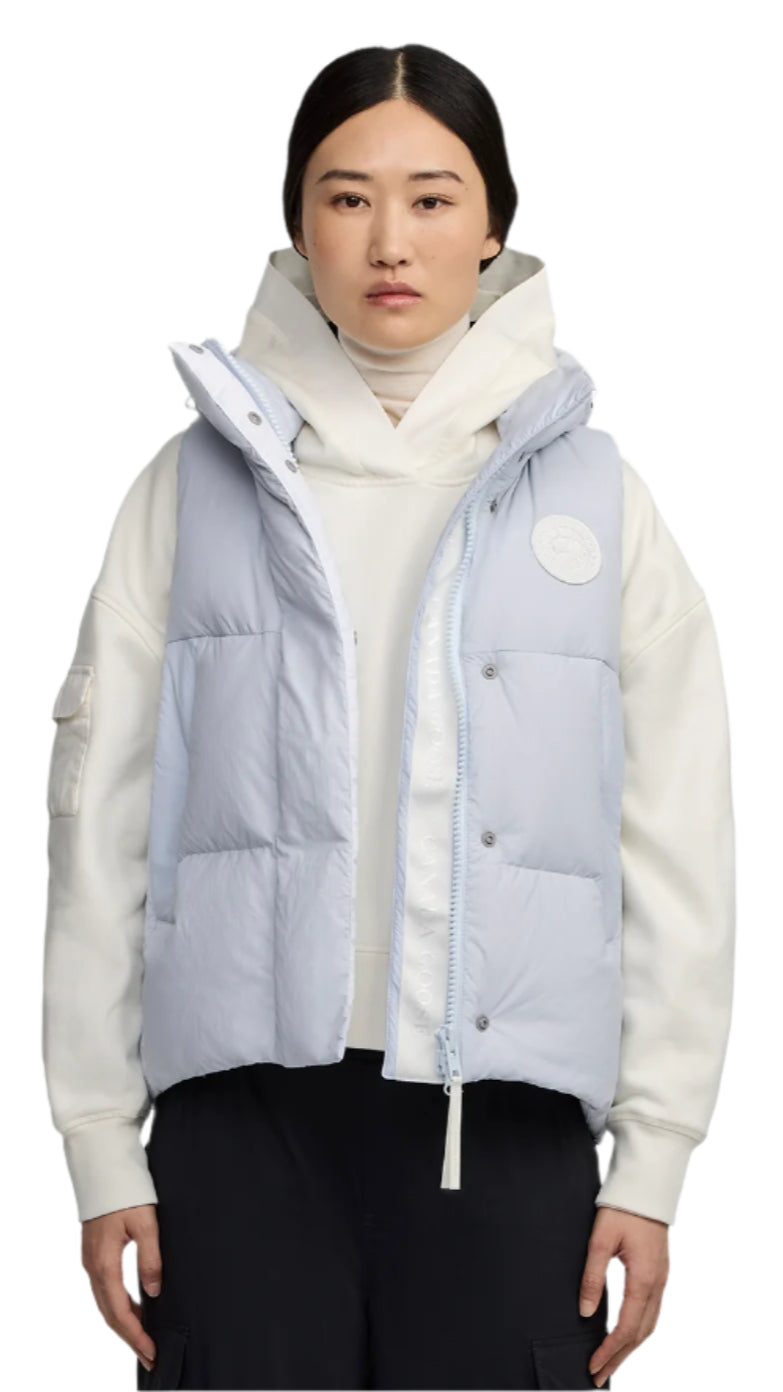 A woman wears a light blue puffy vest over a white sweatshirt with black pants.