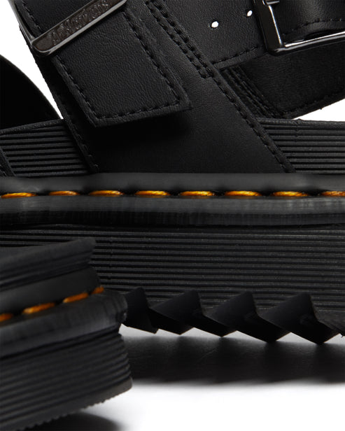 Close-up of black leather sandal featuring buckle strap and thick, ridged sole with yellow stitching.