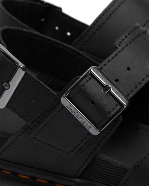 Close up of a black sandal with metal buckle, and logo visible on it.
