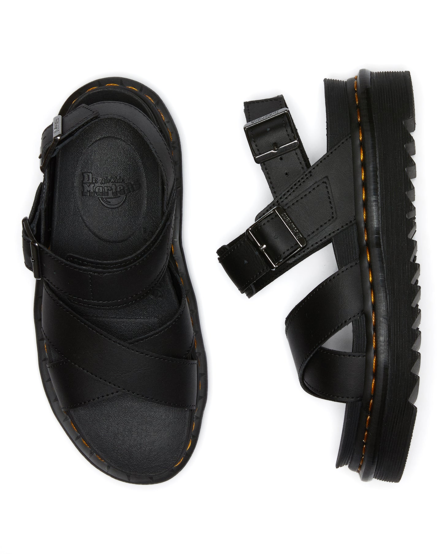 Two black leather sandals with adjustable straps and buckle closures, one lying flat and one standing on its side to show the thick sole with yellow stitching.
