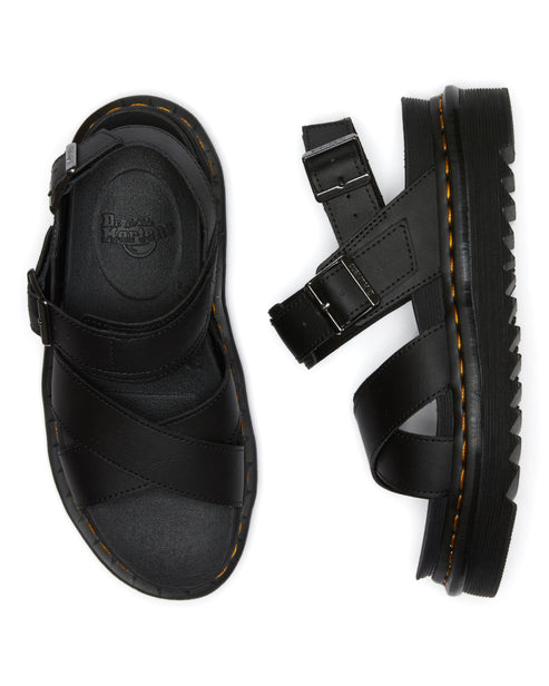Two black leather sandals with adjustable straps and buckle closures, one lying flat and one standing on its side to show the thick sole with yellow stitching.