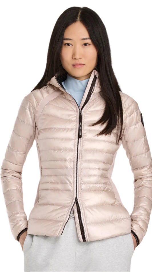 A woman with black hair poses wearing a light pink down jacket with a black zipper.
