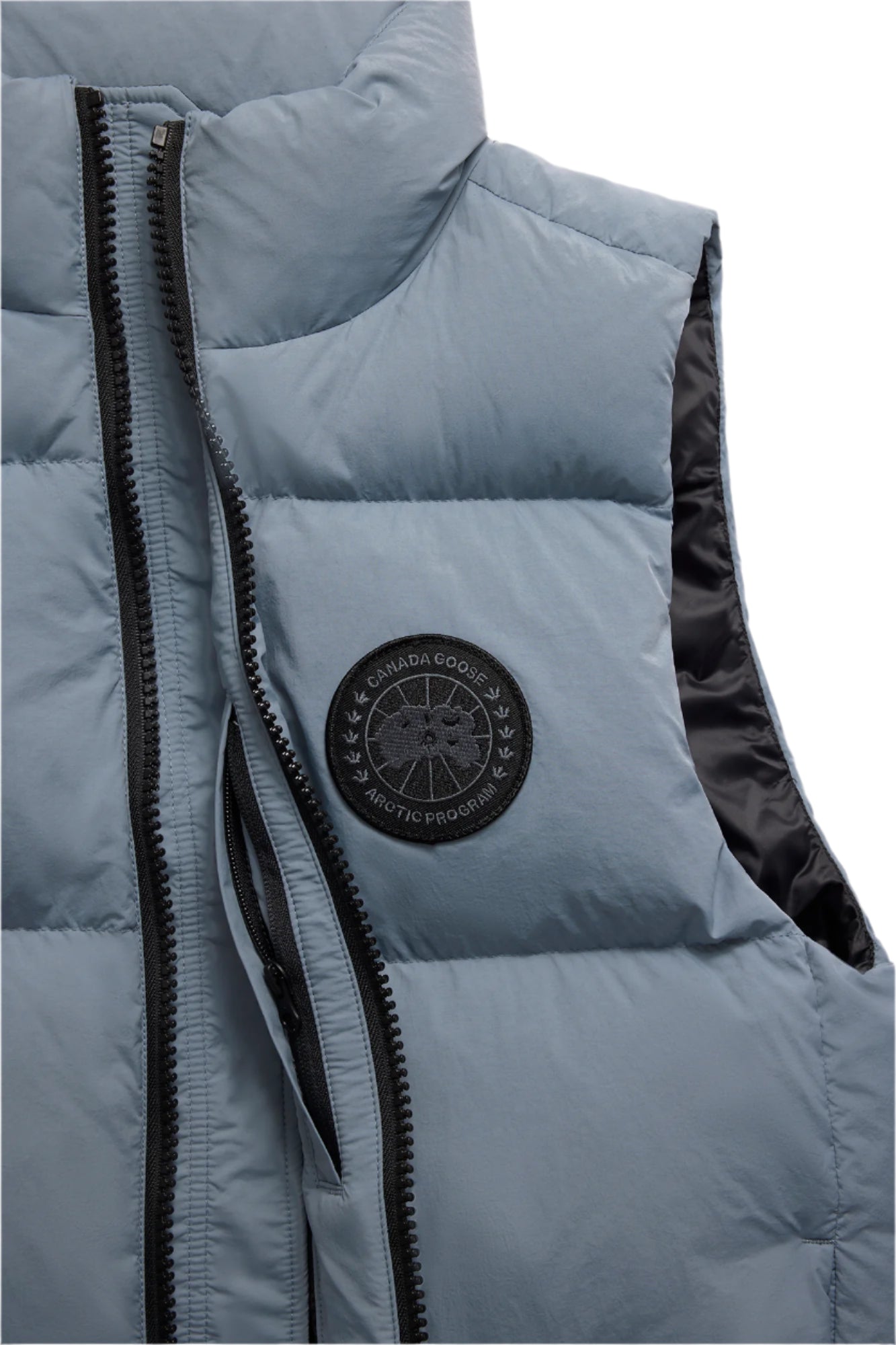 Close-up of a light blue puffer vest with a black zipper and round logo on the upper left chest.