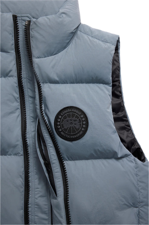 Close-up of a light blue puffer vest with a black zipper and round logo on the upper left chest.