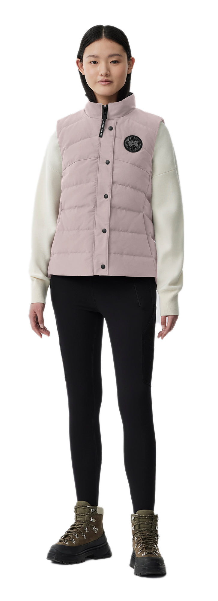 A woman wearing a pink vest, a light-colored long-sleeved shirt, black pants, and camouflage boots.