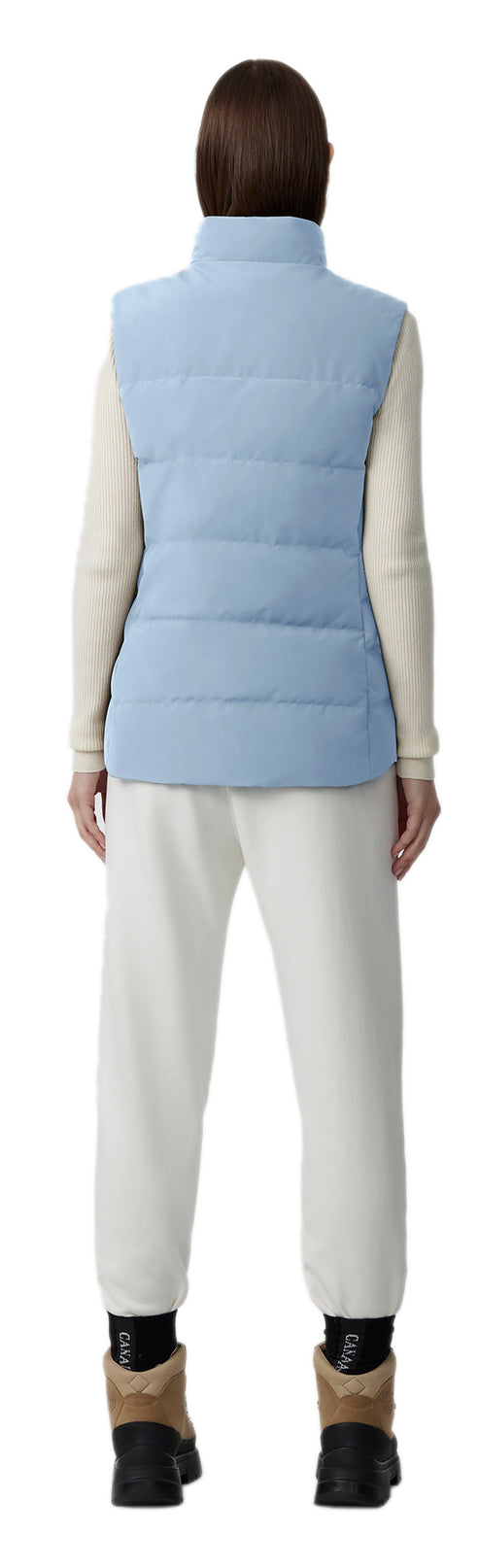 A person is wearing a light blue vest, long sleeve shirt, pants and boots. 