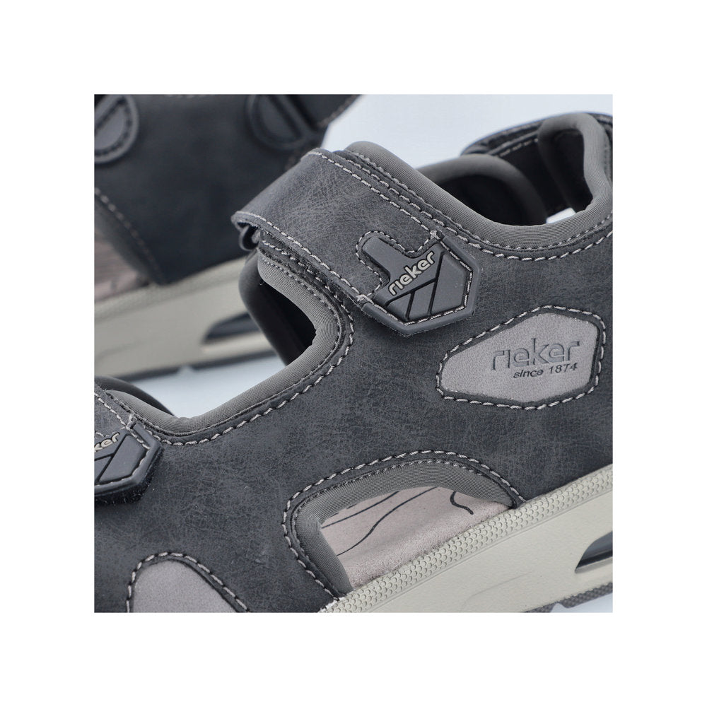 Close-up of a gray sandal with hook and loop closure. 'Rieker' brand logo is visible on the side.