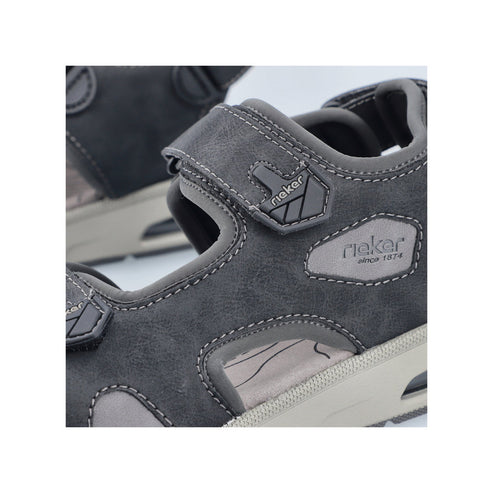 Close-up of a gray sandal with hook and loop closure. 'Rieker' brand logo is visible on the side.