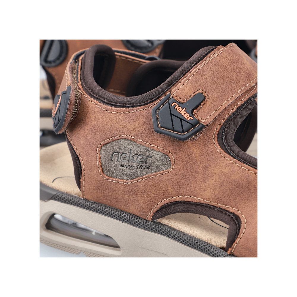 Close-up of a brown sandal with velcro strap and the word 'rieker since 1874' visible.