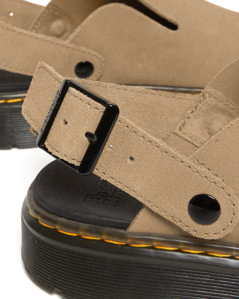 Tan suede sandal with an adjustable buckle strap on a black sole with yellow stitching.