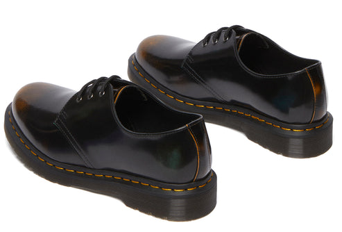 Pair of glossy black shoes with yellow stitching, low angle view.