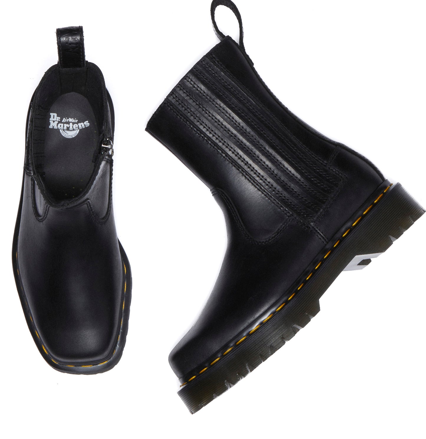 Two black, ankle-high boots with yellow stitching around the soles. One boot is sideways, showing a square toe, side elastic panel, and ridged vamp. The other boot has a zipper, and its interior shows a logo.