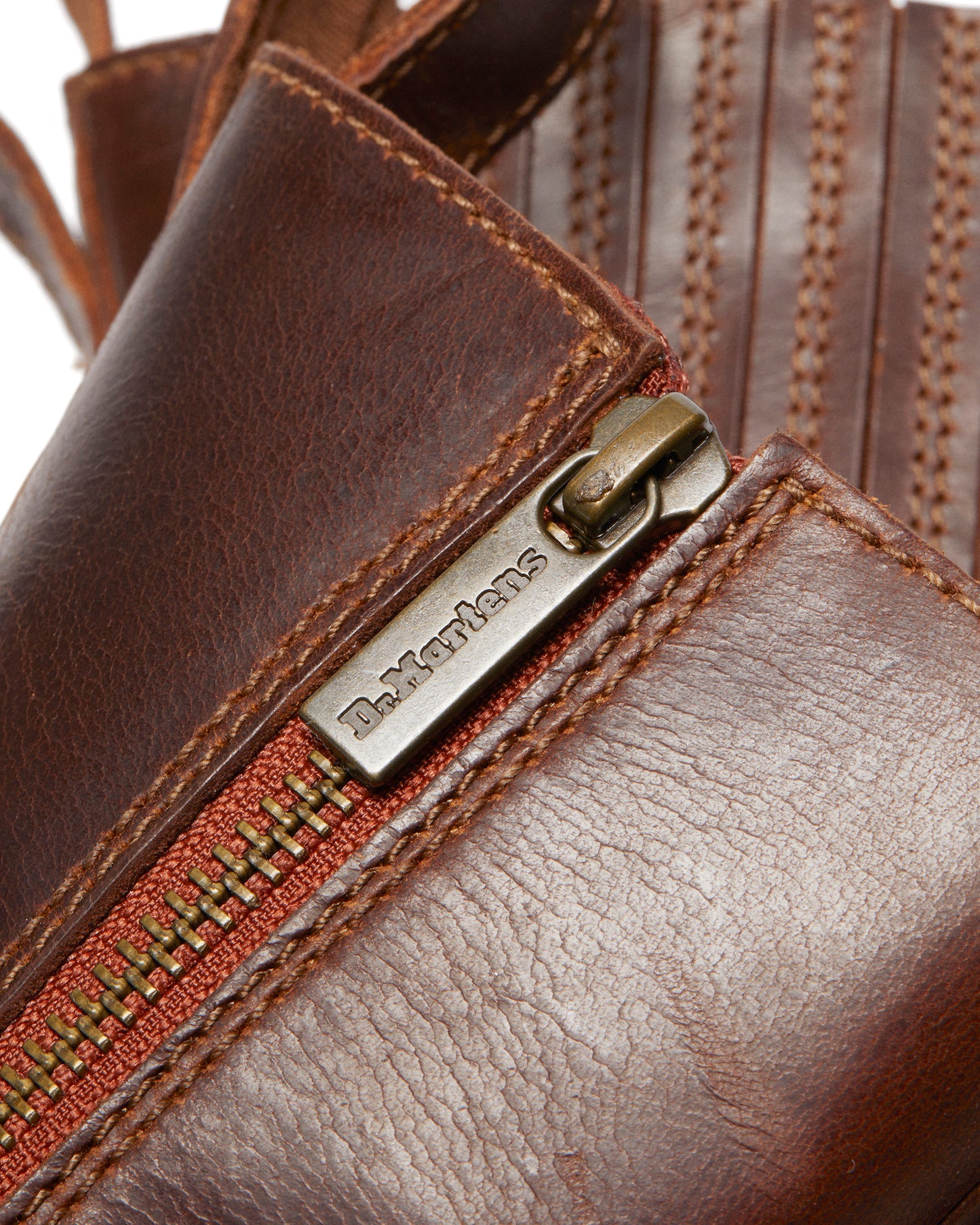 Close-up of a brown leather boot featuring a metallic zipper with 'D. Martens' engraved on the pull tab.