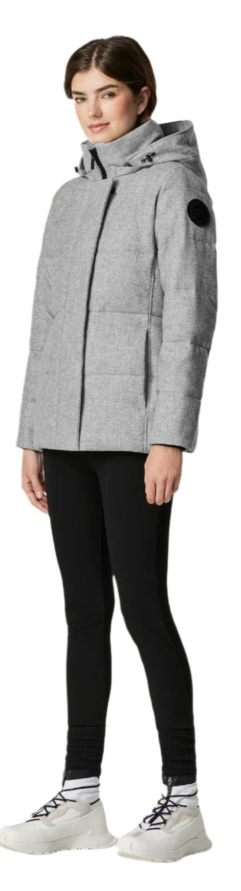 A woman in a gray puffer jacket, black leggings, and white sneakers.