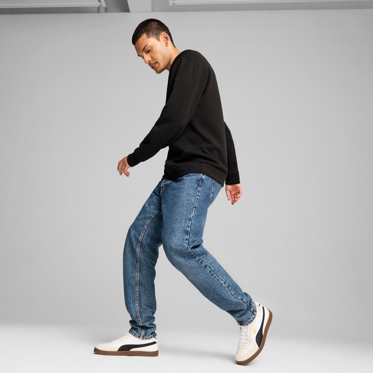 A person wearing a black long-sleeve shirt and blue jeans, walking and looking down.