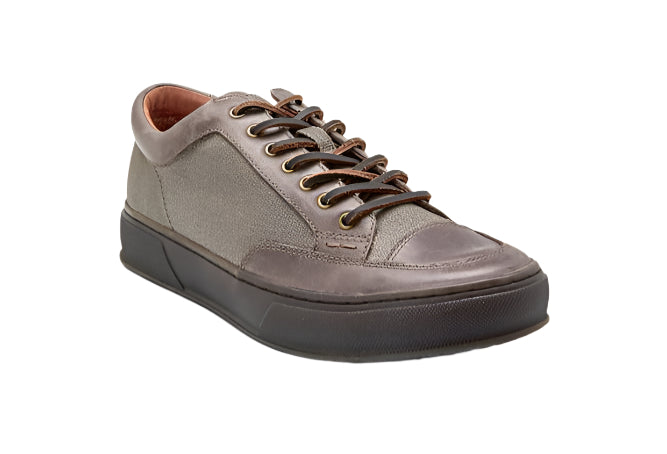 Low-cut sneakers with brown laces and a weathered gray leather upper, placed on a dark sole.