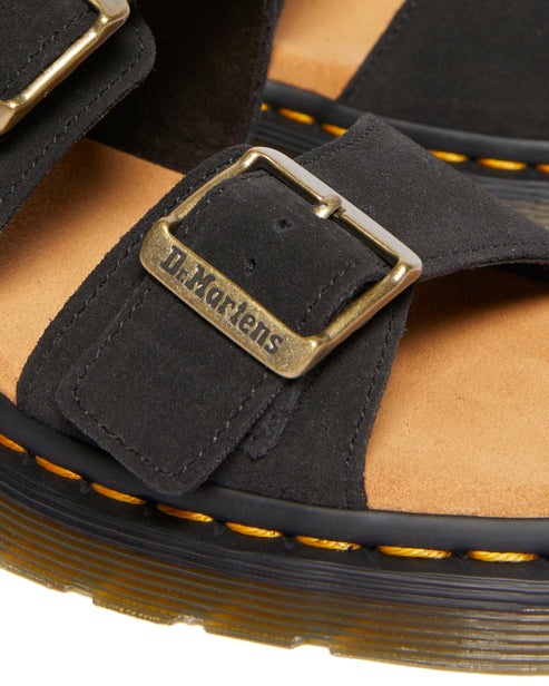 Close-up of black suede sandal with brass buckle displaying the text "Dr. Martens".
