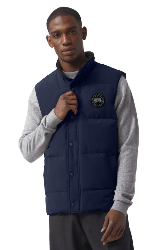 A man wearing a navy vest with a circular logo on the upper left chest.