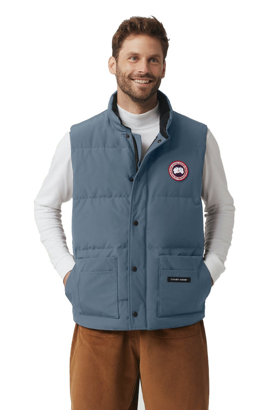 Man wearing a blue vest with the logo on the chest over a white long-sleeve shirt.