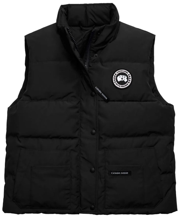 A black, sleeveless, quilted, insulated down vest with a stand-up collar, a zipper closure hidden by a snap-button placket, a circular embroidered logo patch on the left chest, and a small black rectangular patch with white text reading "CANADA GOOSE" on the bottom right pocket.