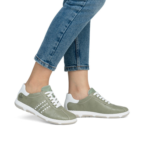 Light green leather sneakers with white soles and white laces on model.