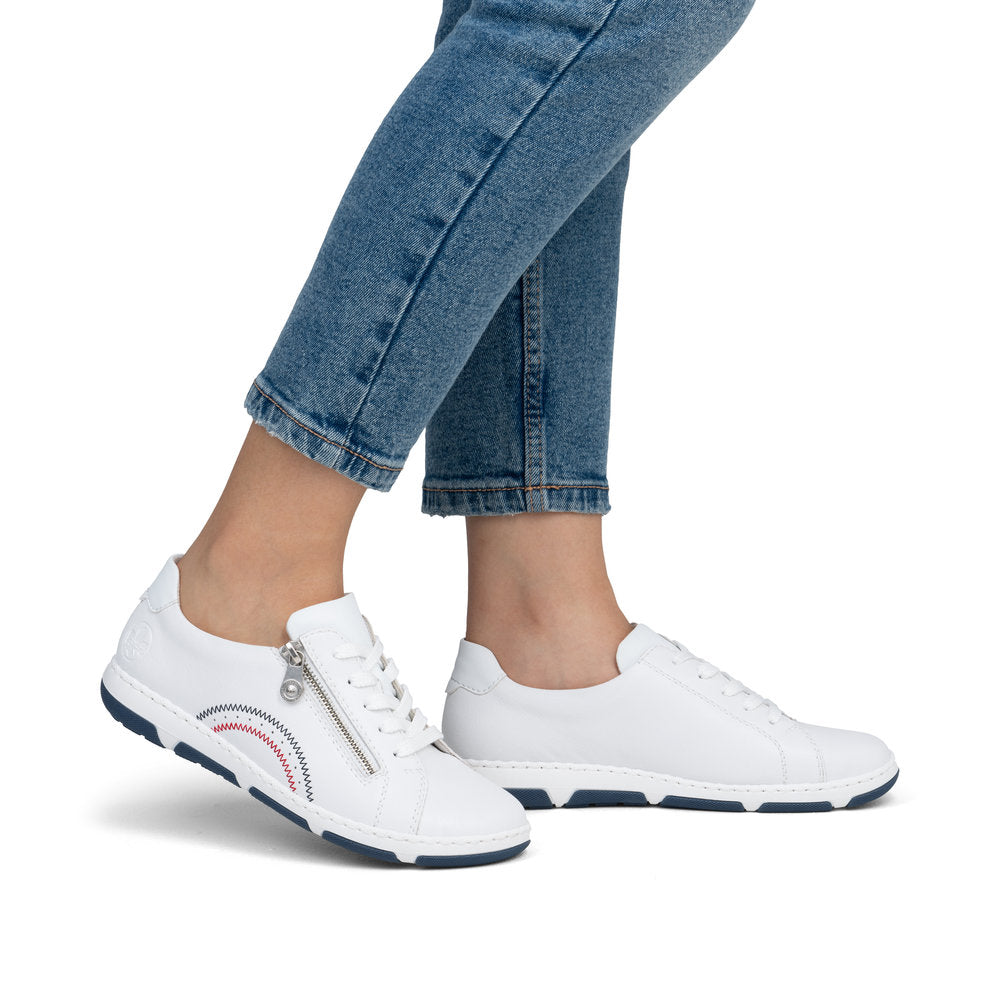 Low-top white leather sneakers with zipper closure, worn with blue jeans.