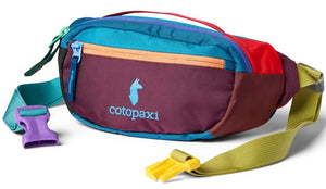 A colorful fanny pack featuring a dark maroon front panel with a light blue llama logo and the text 'cotopaxi' printed below. The pack has a bright teal upper section, red and olive-colored sides, and an orange zippered pocket. It includes an adjustable olive green strap with a purple plastic buckle on one side and a yellow plastic buckle on the other, along with a teal handle on top.