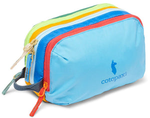 A colorful nylon travel pouch with a light blue front panel featuring a blue llama logo and the text cotopaxi, followed by multi-colored zippered sections in red, blue, yellow, and green, with several zipper pulls and a small side handle.