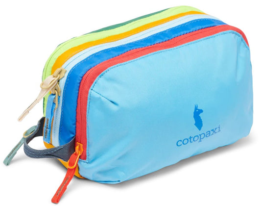 A colorful nylon travel pouch with a light blue front panel featuring a blue llama logo and the text cotopaxi, followed by multi-colored zippered sections in red, blue, yellow, and green, with several zipper pulls and a small side handle.
