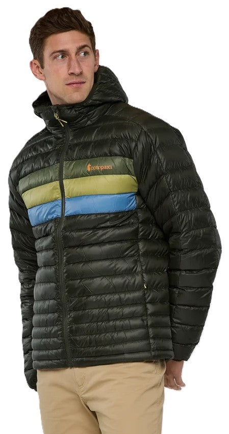 A man wearing a black hooded puffer jacket with a horizontal band of olive green and sky blue stripes across the chest and khakis.