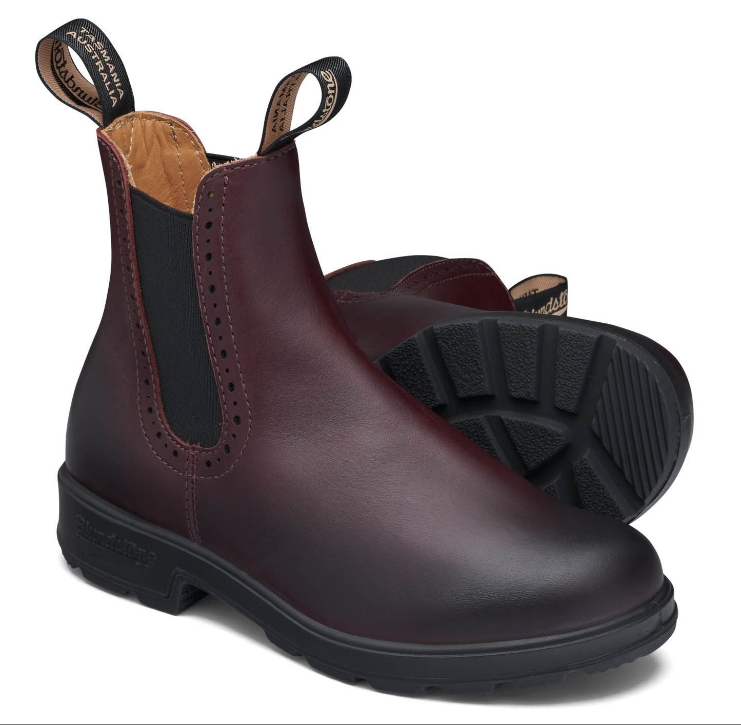 A pair of burgundy, ankle-high boots with black elastic side panels and black soles, with perforations near the elastic.