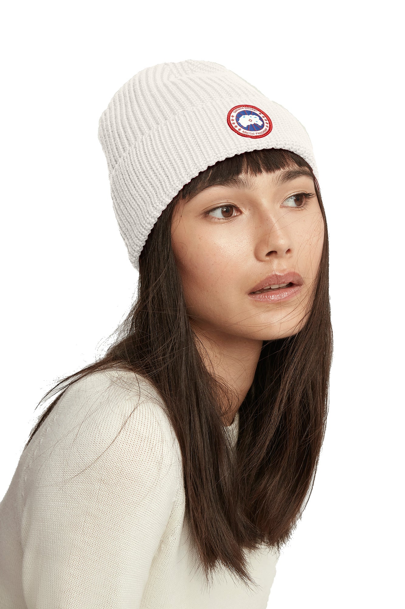A woman with dark hair wearing a white ribbed beanie with a circular logo.