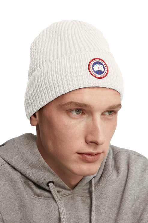 Person wearing a white ribbed beanie with a circular red, white and blue logo on the brim.