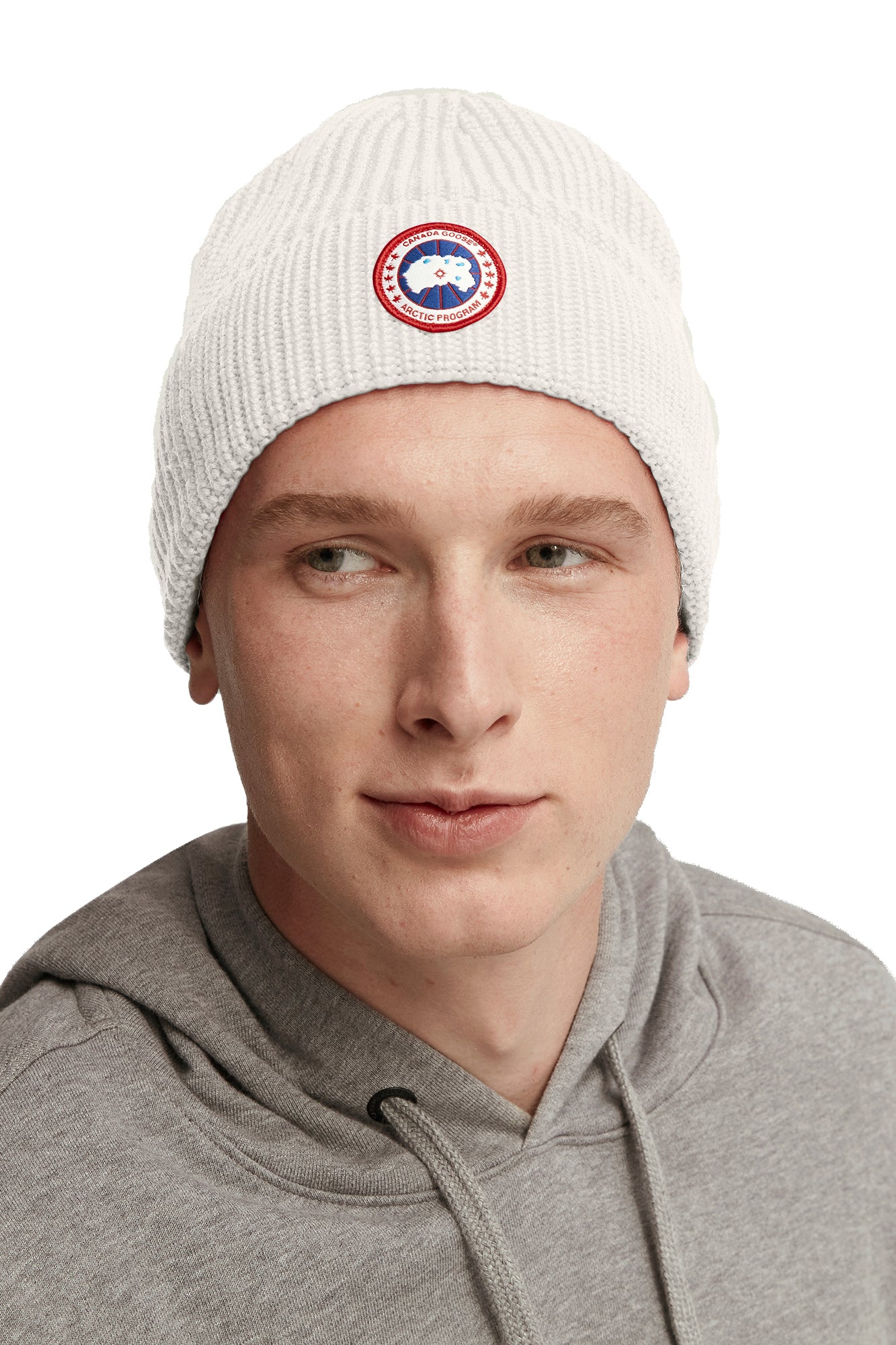 A person wearing a white knit beanie with a round emblem.
