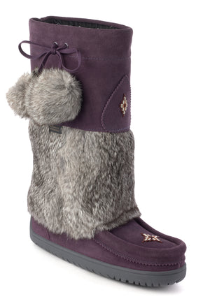 Knee-high purple suede boot with faux fur, pom poms, and a moccasin toe.