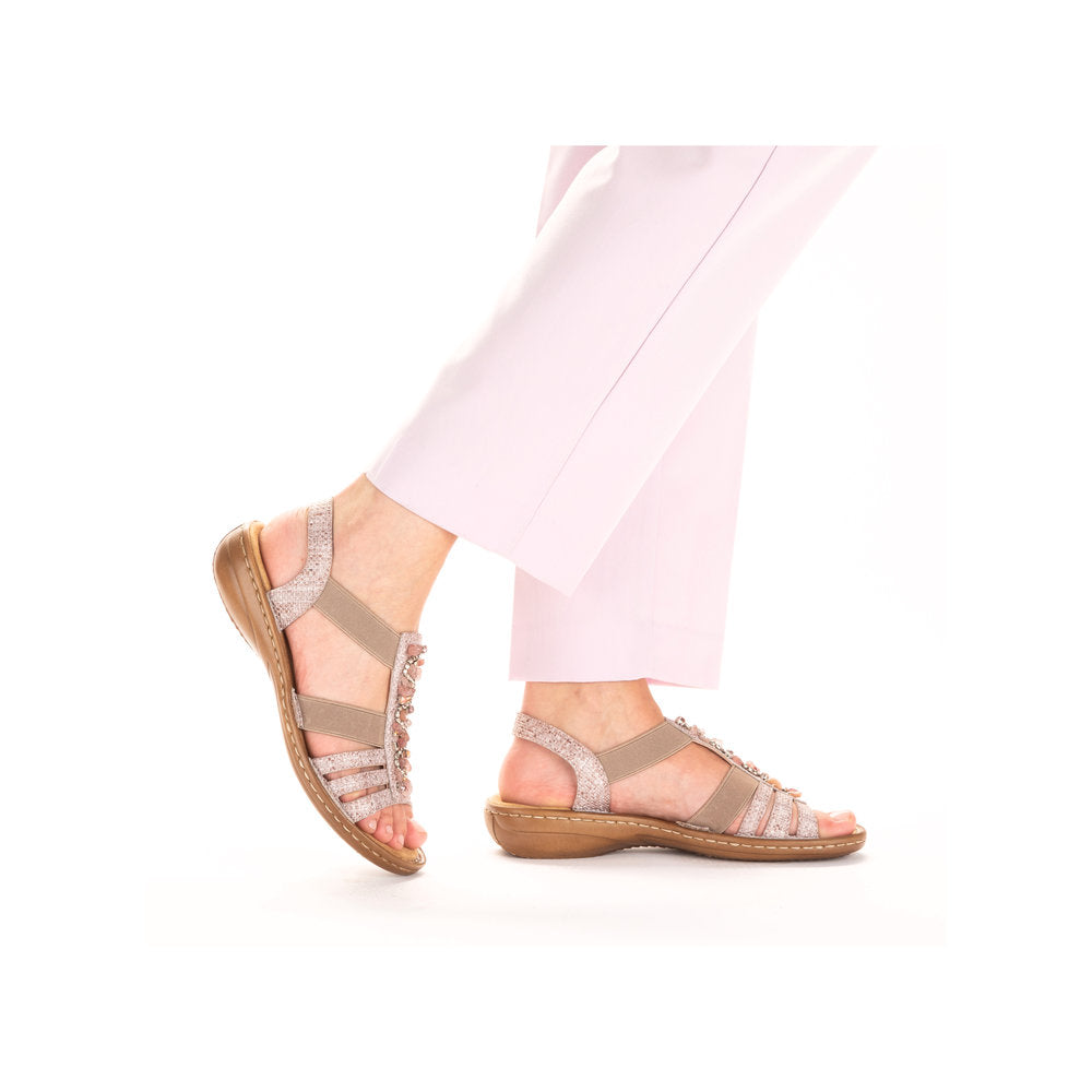 A person wearing tan sandals with decorative beads and pink pants.