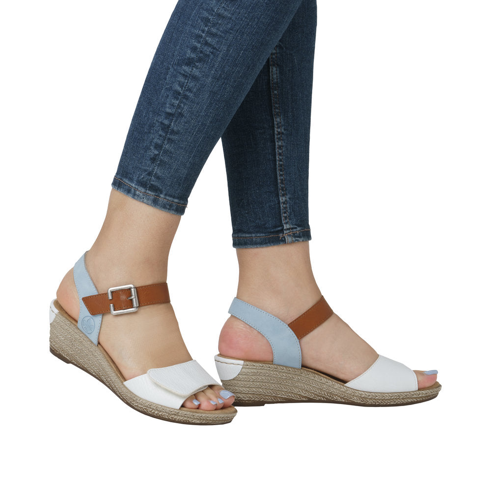 A woman wears open-toed wedge sandals with a white toe strap, brown ankle strap, light blue heel strap, and a silver heel.