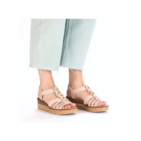 Person wearing beige wedge sandals with a round embellishment.