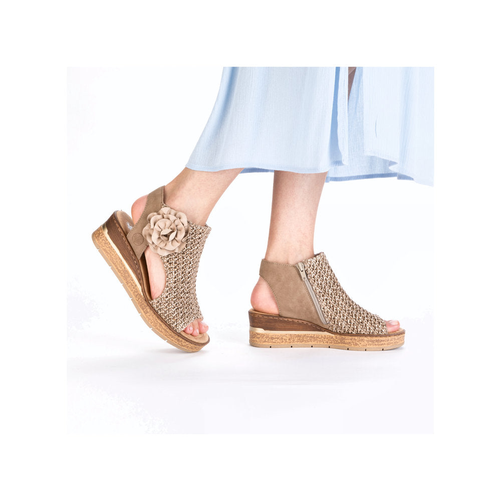 A pair of beige wedge sandals with woven detail, flower accent and side zipper closure.