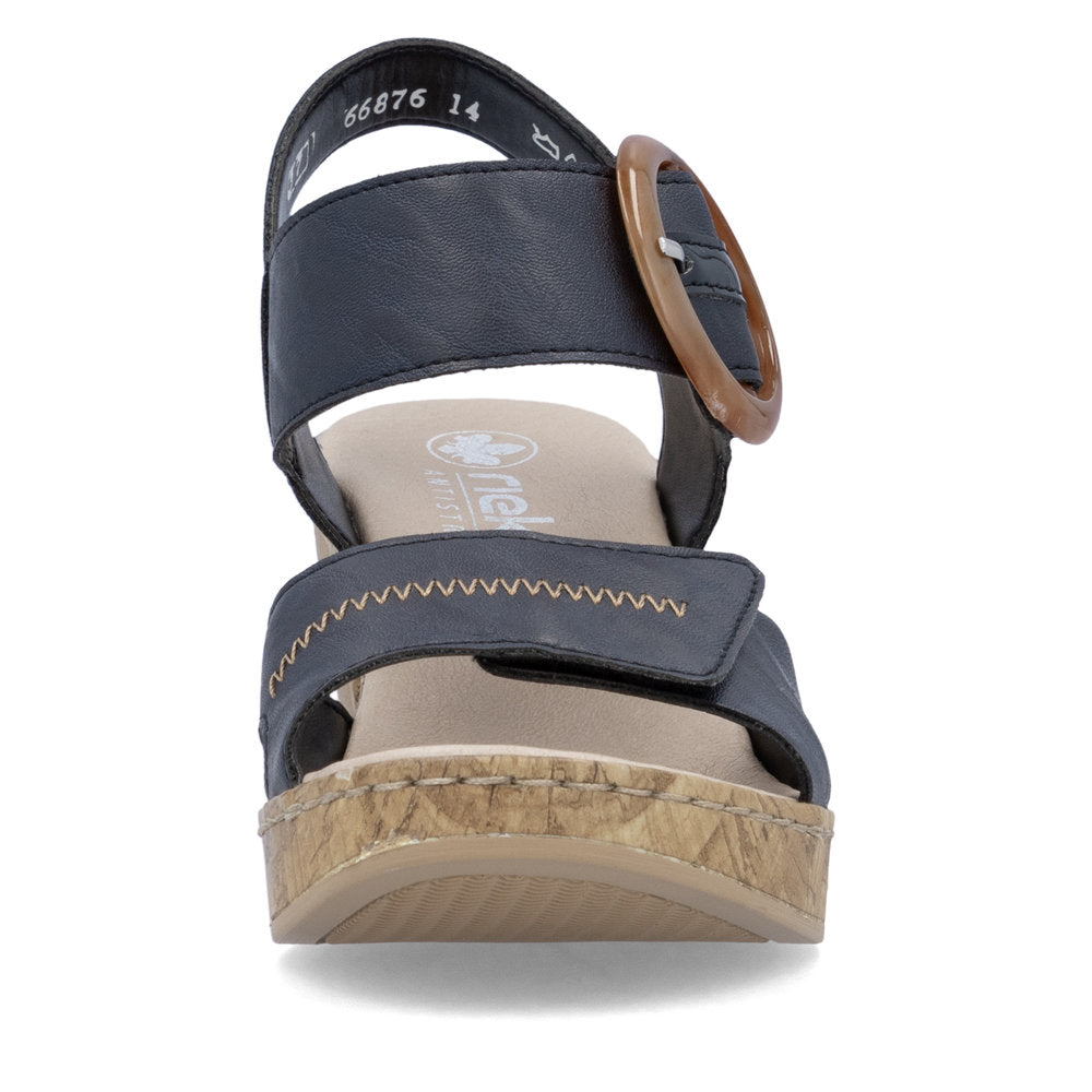 Front view of a blue wedge sandal with a circular brown buckle. The sandal has a light brown cork-like sole.