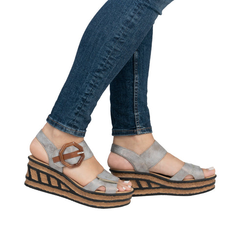 Woman wearing grey wedge sandals with a brown buckle