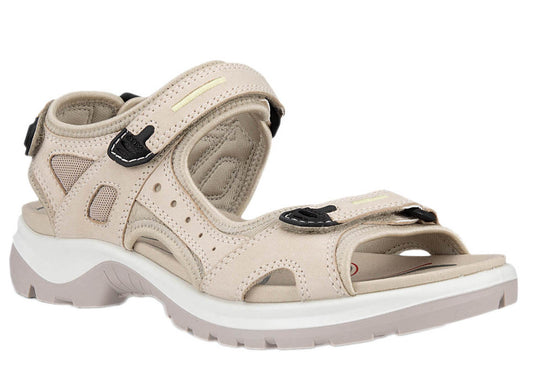 A tan sandal with adjustable velcro straps, white midsole, and black accents.