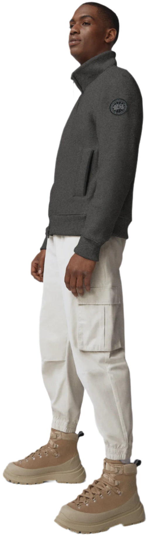 A man wears a gray jacket, beige cargo pants, and beige high top boots.