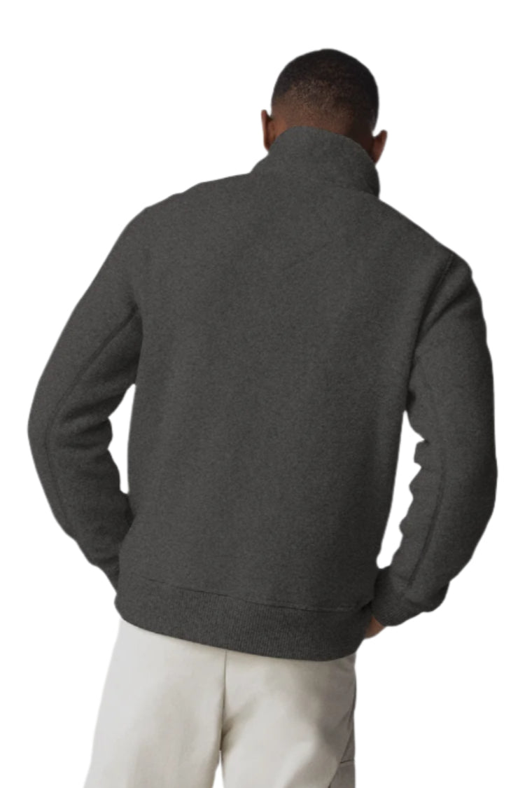 Rear view of a man wearing a charcoal gray sherpa jacket and cream-colored pants.