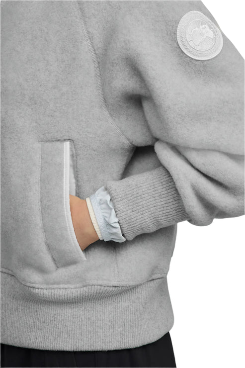 Close-up of a light gray jacket with a white circular patch on the sleeve and a hand in the side pocket.