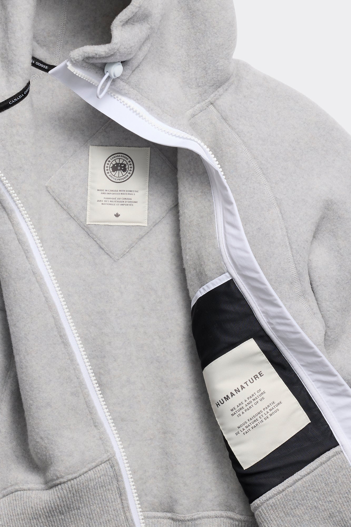 Grey fleece hoodie with white zipper, hood drawstring, and a patch on the chest and inside.