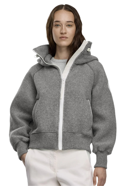 Woman wearing a gray, hooded, wool-blend zip-up jacket with white trim and white pants.